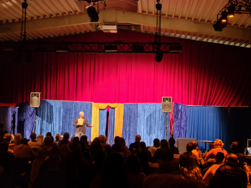 Inno van de Magic Dudes treedt op voor een zaal in Kortrijk. Podium show met een honderdtal mensen die aandachtig kijken naar de show.